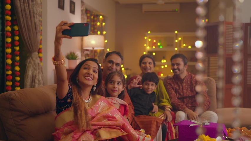 Happy smiling Hindu ethnic Indian family members in traditional attire posing to take or click a selfie picture or photo together using a mobile phone or smartphone during Diwali festival season.	 | Shutterstock HD Video #1095759291