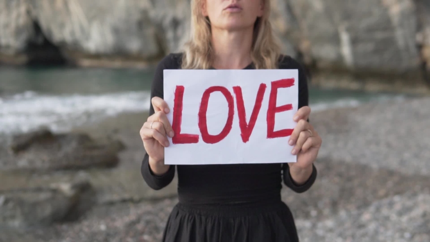 Close-up, a woman standing by the sea with a sheet of paper with the inscription LOVE