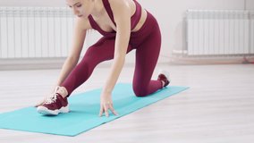 a beautiful and athletic girl in a burgundy tracksuit does gymnastics on the mat in the fitness room. clothes and shoes for gymnastics. professional trainer. fitness