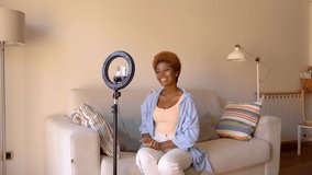Blogger content creator woman sitting on sofa in living room looking at screen of her phone. Using round lamp lighting for video recording for social media. Video footage. Smiling looking at camera - Powered by Shutterstock - Get 15% off with code: PIKWIZARD15