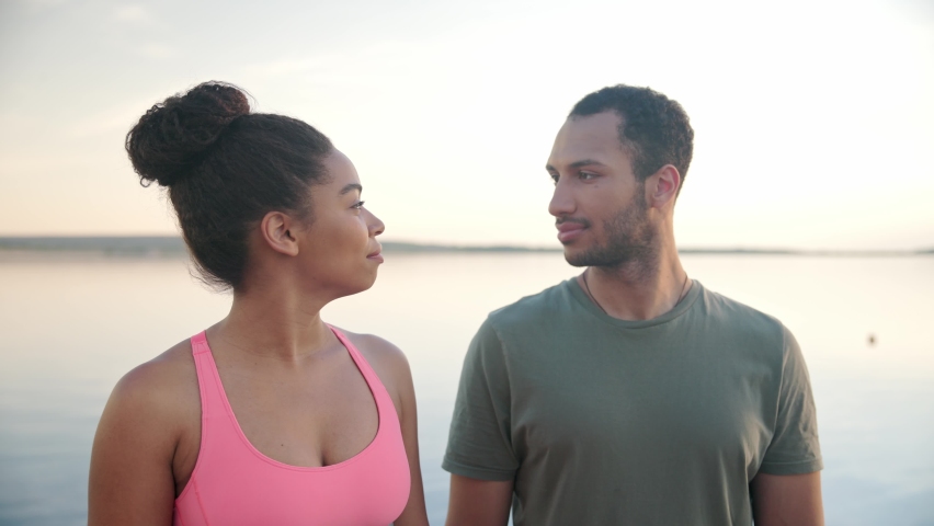 Close up portrait of African American young smiling beautiful woman and handsome man looking at camera standing on nature on lake. Positive couple outdoor on lake on dock. Sky on background