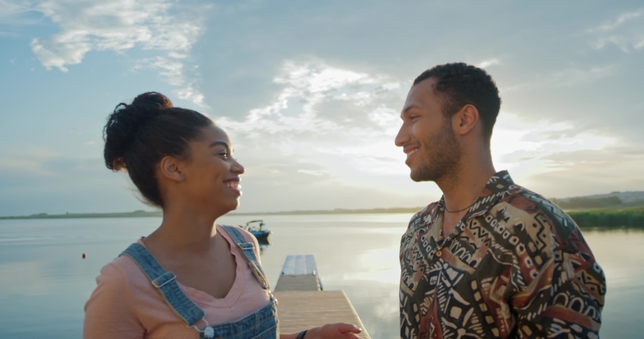 Close up of joyful couple stands on dock near lake looking at each other and chatting then smiling at camera. Nature beauty. Love relationship. Happy man and woman speaking in good mood. Love concept