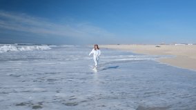 Young woman running along the Atlantic ocean, having fun and laughing. Girl enjoying the ocean waves on a deserted beach. Full HD slow motion video.