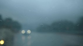 Glass rain auto. A car ride in a heavy downpour. Blurry traffic on the road, headlights of oncoming cars out of focus. The concept of bad weather, storm, hurricane. A gray, rainy, dreary autumn day.