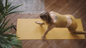 Top view of a sporty woman holding an online stretching workout using a smartphone via video link on a yoga mat.