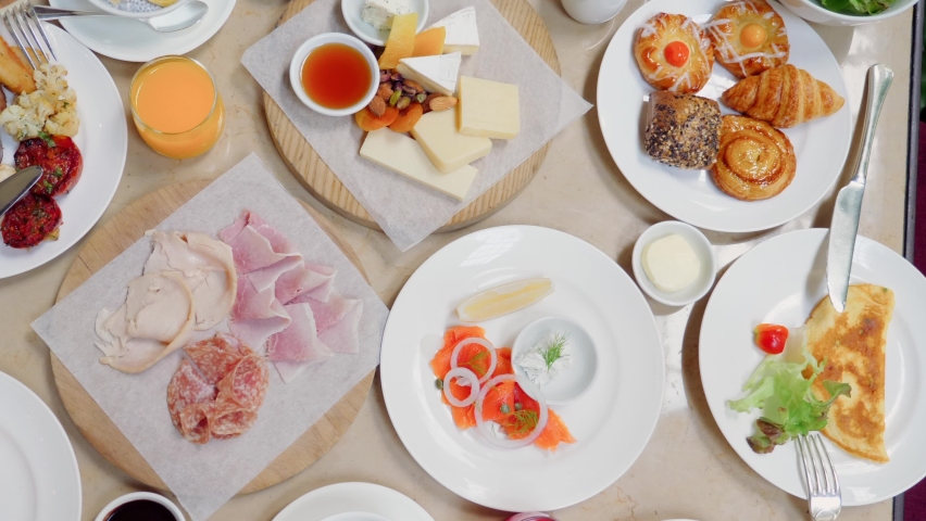 Brunch or lunch in luxury restaurant. Table full of delicious food - cheese, salmon, ham, bakery and juices. Buffet food in hotel. Morning food with various snacks and appetizers. Royalty-Free Stock Footage #1095801881