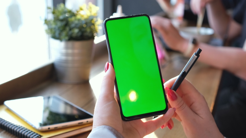 View from shoulder of caucasian woman doing swipe up gesture on chroma key of modern smartphone. Female relaxing in a Chinese restaurant and using cell phone.