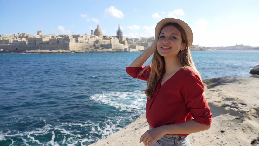 Portrait of young woman on waterfront looking at camera with Valletta city on the background, Malta Island