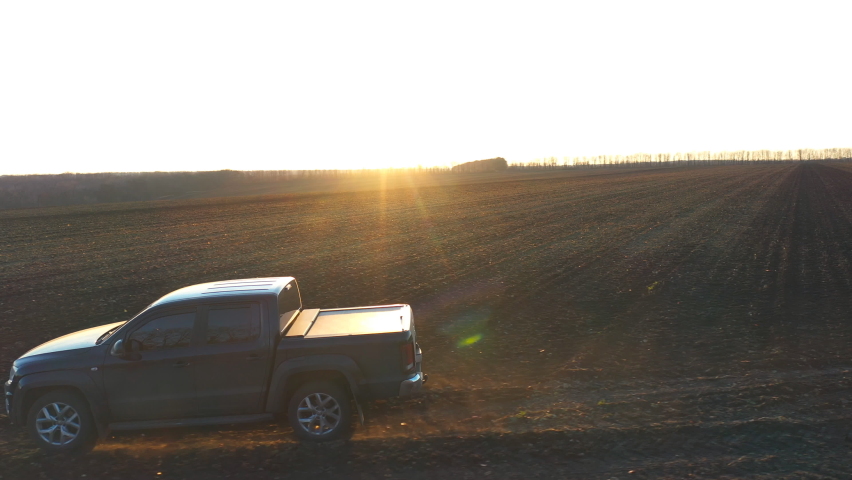 Pickup truck driving through plowed field with sunlight at background. Off road vehicle riding along ploughed meadow. Black car going on route at early spring. Concept of agronomy farming. Aerial shot Royalty-Free Stock Footage #1095814409