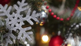Close-up Christmas tree with beads, balls, shape of snowflake, bow and garland, panoramic camera pan to right, on background of Christmas tree with decorations in blur.
