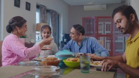 An Indian South Asian ethnic happy elderly woman or grandmother along with an old man or grandfather is feeding a portion of food to a cute granddaughter or kid girl at the dining table during lunch.  - Powered by Shutterstock - Get 15% off with code: PIKWIZARD15
