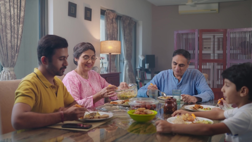 An entire happy Indian South Asian ethnic loving family members including parents, grandparents, and kids or children are having lunch, or a meal together in an indoor home. Relationship, food concept Royalty-Free Stock Footage #1095816777