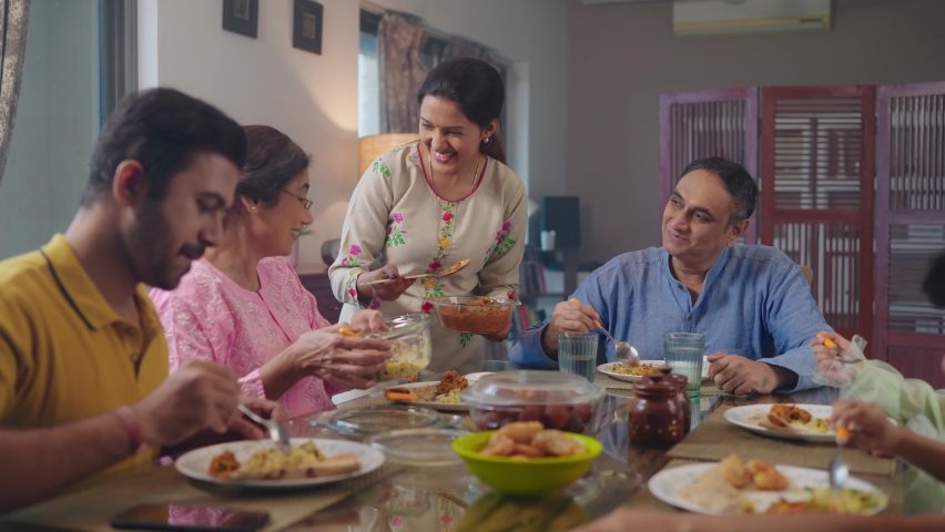 An entire happy Indian South Asian ethnic loving family members including parents, grandparents, and kids or children are having lunch, or a meal together in an indoor home. Relationship, food concept