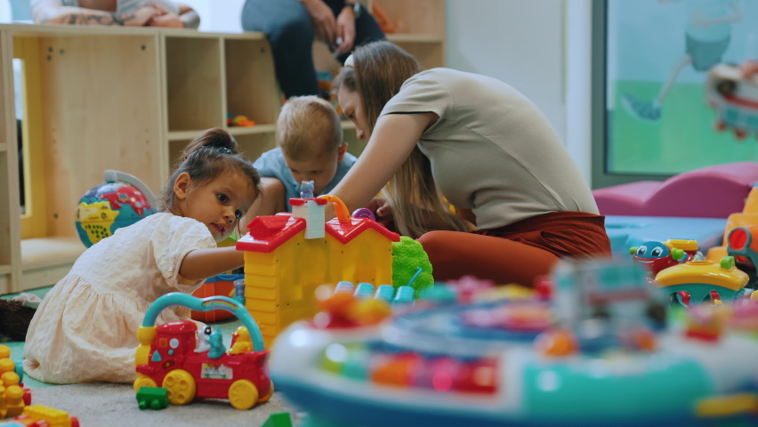 Multiracial group of little children playing with various colorful toys with their daycare teacher. Nursery playtime. Horizontal indoor shot. High quality 4k footage Royalty-Free Stock Footage #1095817611