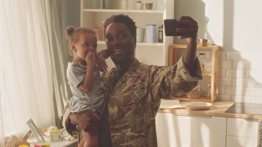 Cheerful African American man taking selfie portrait on smartphone with his pretty toddler girl holding her in arms at kitchen | Shutterstock HD Video #1095818259