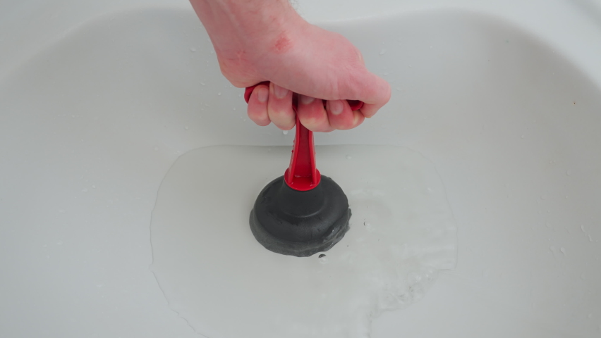 hand with plunger unclog clogged sewer. clearing clogged drain. ceramic sink drain hole blockage problem solution. use plunger sink cleaning drain pipe blockage. uncork clogged sewage in bathroom sink Royalty-Free Stock Footage #1095821065
