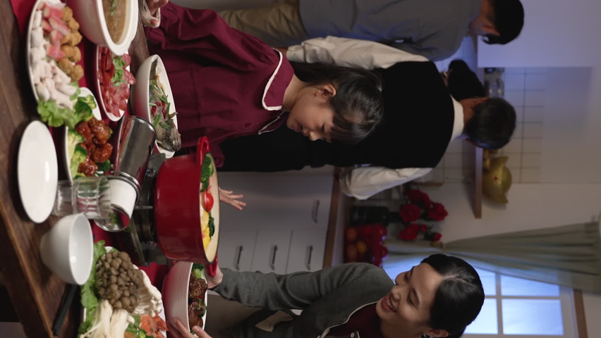 Vertical Screen: granddad and mom talking to granddaughter by dining table and looking at family members together preparing for chinese new year