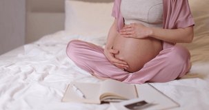 pregnant woman touching belly and sitting on the bed