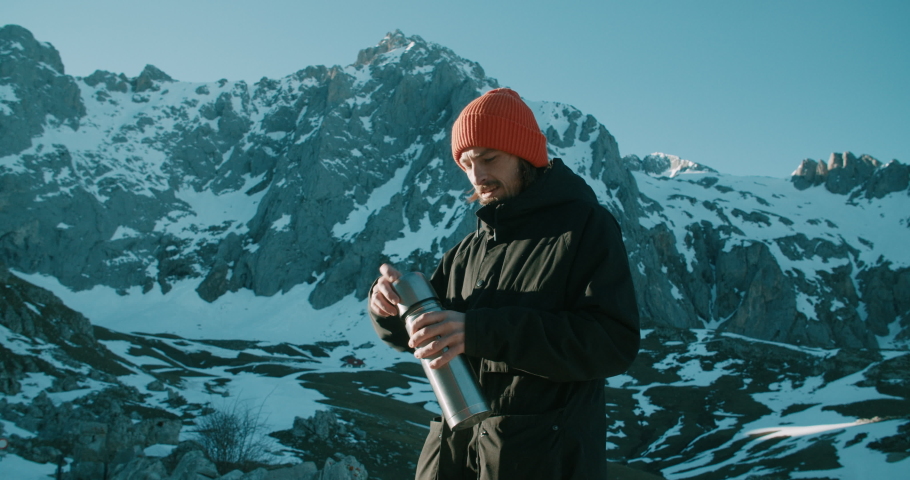 Male traveler on hike journey adventure taking break and pouring hot drink from thermo to the cup on epic mountain landscape. Contented successful man on mountain peak at winter travel | Shutterstock HD Video #1095826573