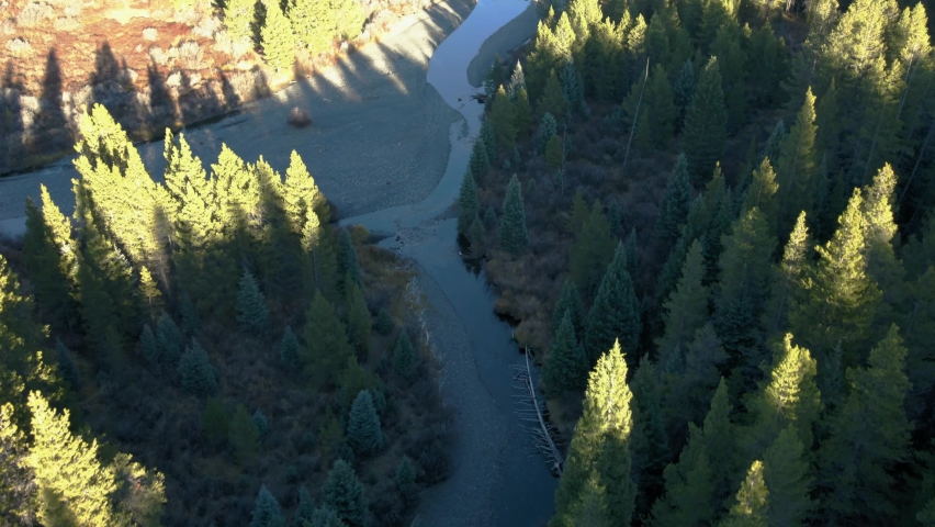 A drone flyover of a shallow creek near Oh Be Joyful campground in Crested Butte Colorado at sunset in the fall months - mountains and evergreen trees can be seen in the background during golden hour