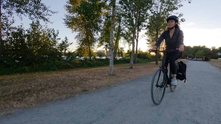 Adventure Woman bike riding on a bicycle trail surrounded by green trees. Summer Sunset. Pitt Meadows, Greater Vancouver, British Columbia, Canada.