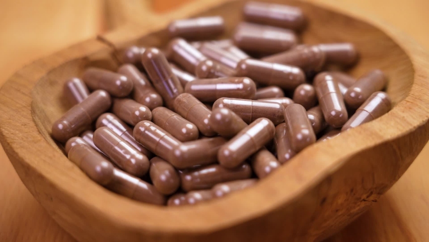 Vitamin nutritional supplement capsules falling into a wooden rustic container on a woody brown background in slow motion. Dietary pills close up. Alternative medicine concept