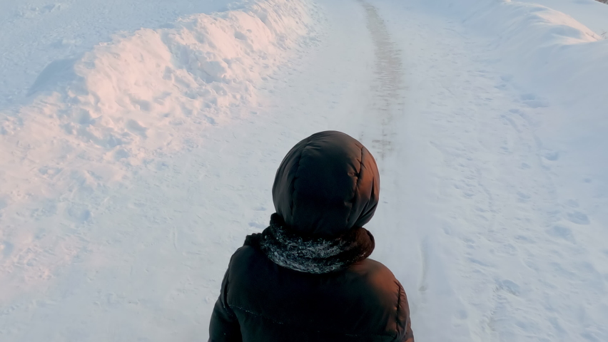 Teenager sliding on snow covered slope at sunset. Rear view of child is enjoying on white landscape. She is having fun during winter vacation.