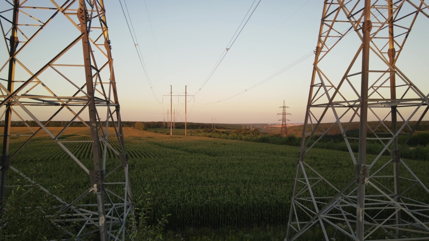 Electricity pylons. Moving between row of pylons. electric high voltage pylon against sunset sky. Aerial wide footage Royalty-Free Stock Footage #1095847731