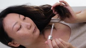 Split Ends Care. Smiling Asian Woman Applying Moisturising Oil To Her Curly Hair, Closeup Of Young Female Putting Haircare Product With Dropper While Making Beauty Routine At Home.