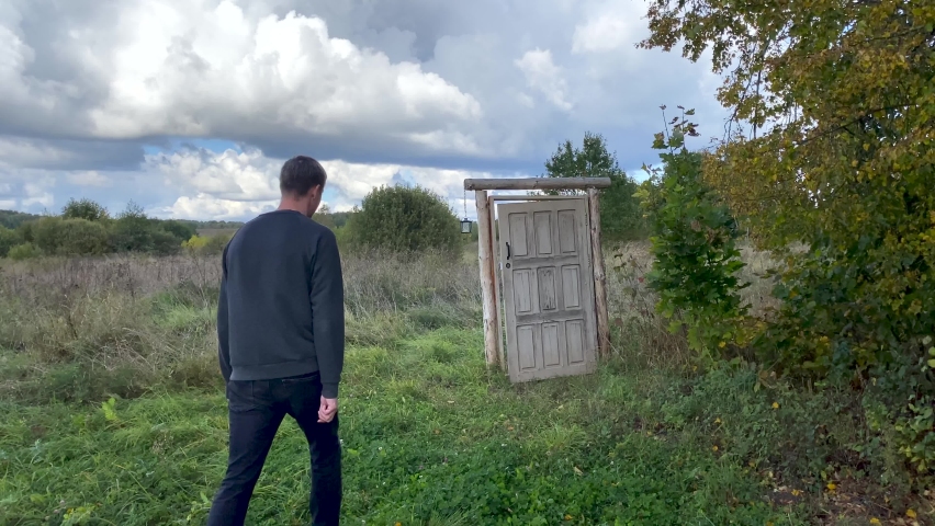 Person exits via the door that leads to nowhere and disappears. Man going through old mystery portal in the open field. Concept of finding a way out, existence of the supernatural or another world Royalty-Free Stock Footage #1095855343