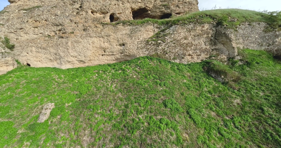 FPV sports drone shot Caucasian equestrian on horse contemplate cliff summer landscape from mountain summit. Aerial view horseman highlander traditional clothes admiring dramatic sky nature scenery