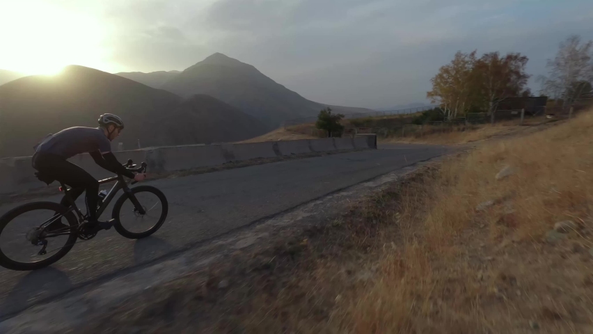 Aerial view athletic sportsman riding asphalt serpentine road sports bike at sunset mountain valley landscape. FPV sport drone shot active man cycling extreme outdoor leisure activity cliff scenery 4k Royalty-Free Stock Footage #1095865473