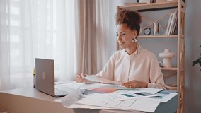 African American woman develops interior design talking to project owner on video call showing examples of colors. Young designer sits at desk near laptop