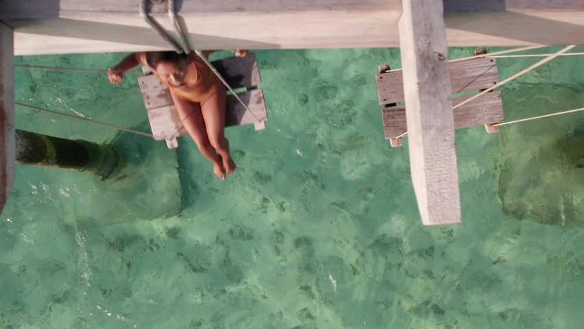 Aerial tilt up shot of young woman on beach swing in ocean. Drone view of transparent clear water and coral reef. Concept of top travel destination Royalty-Free Stock Footage #1095869593