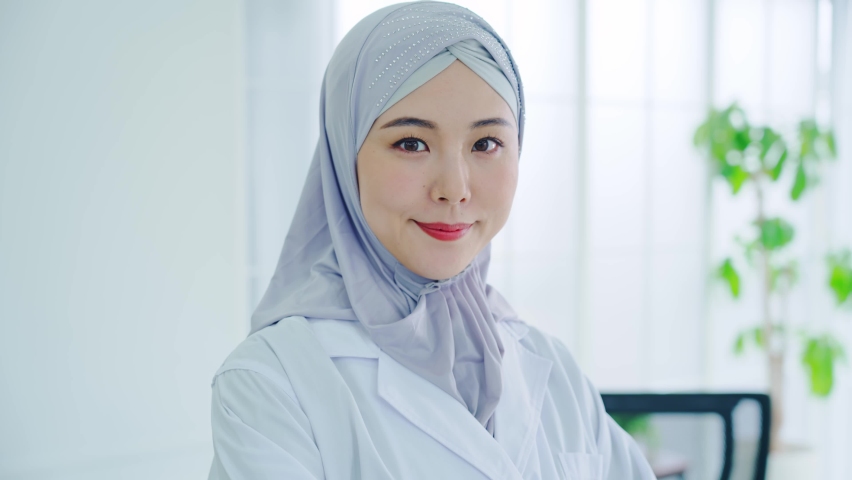 Asian woman in a lab coat wearing a hijab standing in the office.