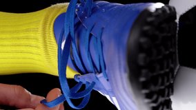 Soccer Player Tying Shoelaces on Football Cleats, Close-up. Athlete's Foot in Football Boots on Soccer Ball. Soccer World Cup. Vertical Video