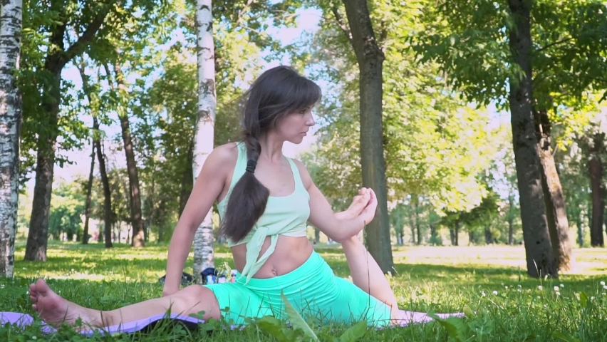 beautiful Brunette woman sportswear trains yoga asana green juicy grass purple mat barefoot, doing lotus for meditation balance body outdoor city park, healthy lifestyle, selective focus Slow motion