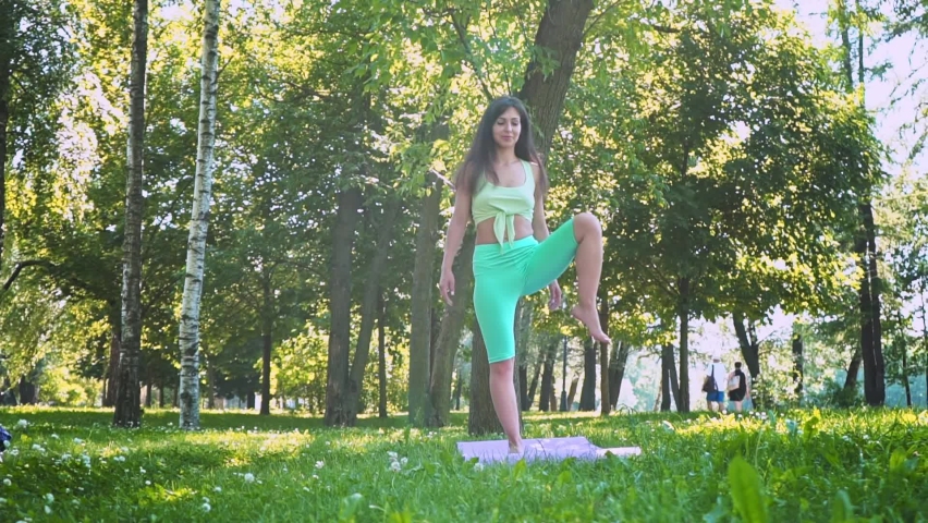 beautiful Brunette woman sportswear trains yoga asana green juicy grass purple mat barefoot, doing lotus for meditation balance body outdoor city park, healthy lifestyle, selective focus Slow motion