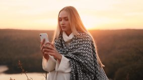 Charming young traveler have a video call with beautiful sunset in the mountains. Young blond woman recording video for her social media blog.
