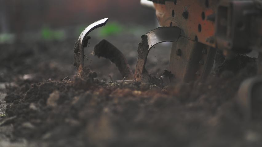 Close-up of process plowing land with machinery. Spinning blades or gears weed field before new seedling of plants. Agriculture food industry. Growing and caring for farmland vegetable bed on field. Royalty-Free Stock Footage #1095888481