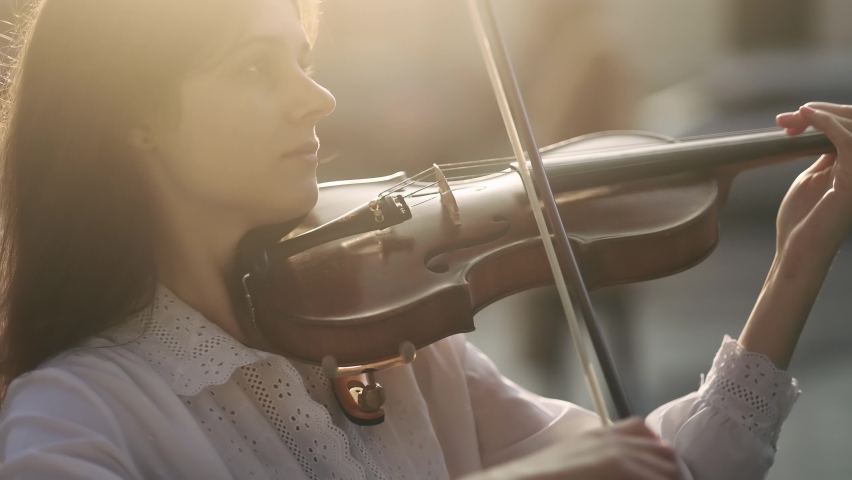 Close up of classical violinist playing a classical wooden violin on the urban city street. Young attractive street musician playing outside with warm sunset light.