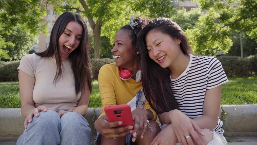 Three happy women using cell phone outdoors. Group of smiling female friends viewing social networks on smartphone. Girlfriends having fun watching something on mobile. Young people flirting online.  Royalty-Free Stock Footage #1095896577