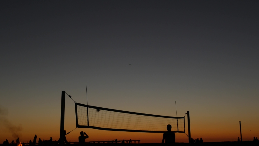 Volleyball net silhouette on beach sport court at sunset, people playing on California coast, USA. Sport field for volley ball game players by ocean shore. Twilight sky of Mission beach, San Diego.