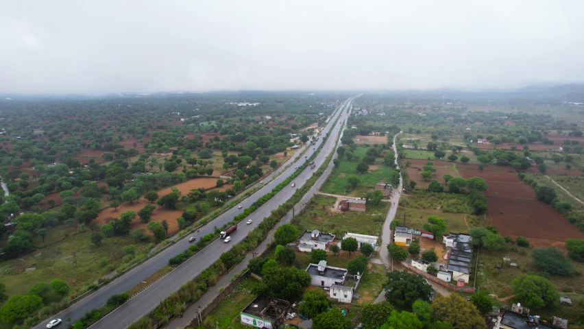 aerial drone shot flying over jaipur delhi highway wet from monsoon rains with vehicles with trucks, cars on it with low cloud cover brushing against aravalli range mountain hills Royalty-Free Stock Footage #1095912465