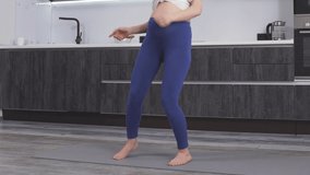 A cheerful pregnant woman with a big tummy dancing to music in her living room, a pregnant woman and sports for pregnant women.