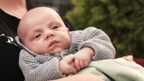 4k footage video. Close up mother hold hands newborn baby child having fun playing, dressed knitted warm sweater, sleepy infant wanted to sleep. Outside walking, fresh air

