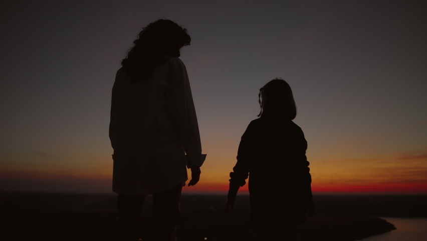 Silhouette of mother and daughter on the background of the sky in the evening after sunset, mother takes her daughter