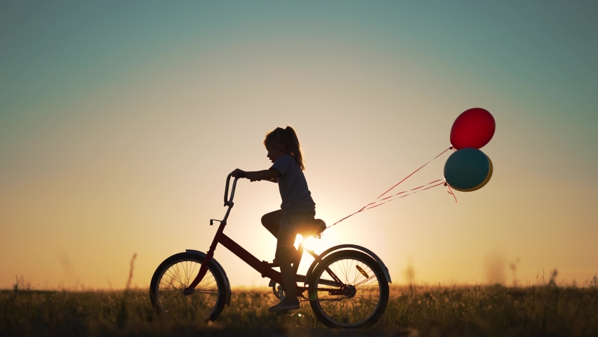 Dream kid. Silhouette of kid on bike in park. Girl rides in park on green grass. Child games in nature.Traveling with balloons on bike.Active child freedom in summer.Girl learns to ride bike in nature Royalty-Free Stock Footage #1095915851