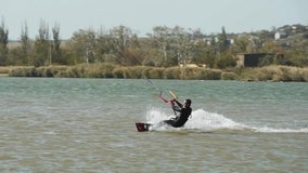 Kiteboarder rides on a kite doing and practicing tricks in sea bay. Freestyle kiter jumping, training on pond kiteboarding spot. Kitesurfer enjoying ride. Extreme water sports. Slow motion 120 fps.