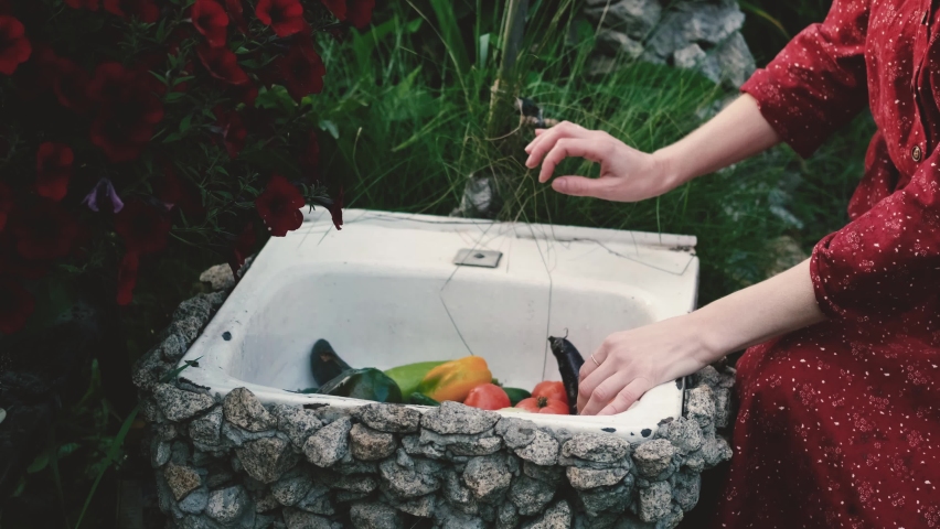 A woman washes vegetables under tap water outdoors. Harvesting vegetables grown on their own.